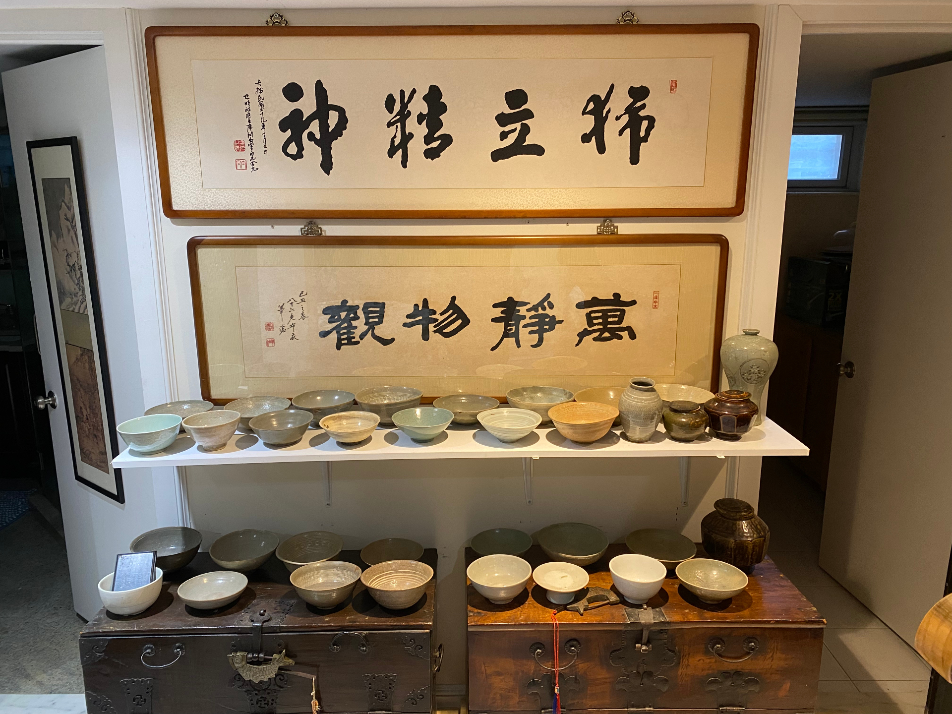 Framed Korean calligraphy above a shelf of celadon bowls and ceramics
